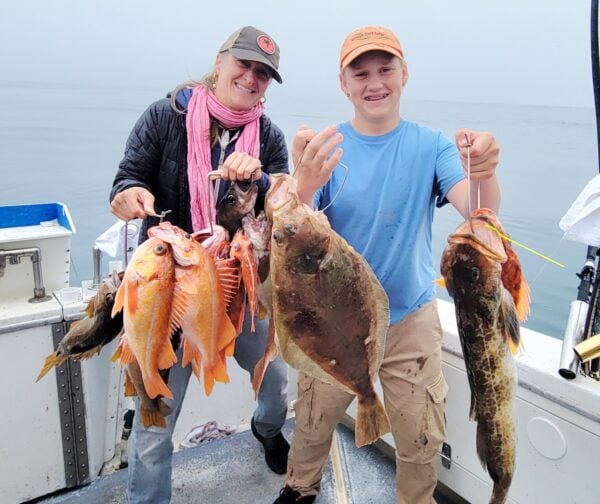 Two people holding caught fish on a boat in Santa Cruz.