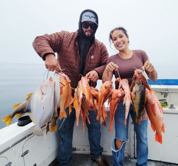 Two people holding a string of freshly caught fish on a boat.