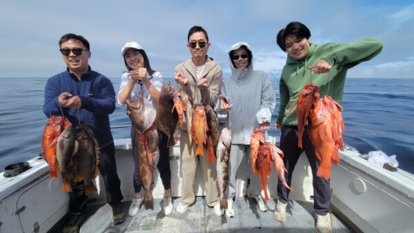 Group of five people holding fish on a boat in the ocean.