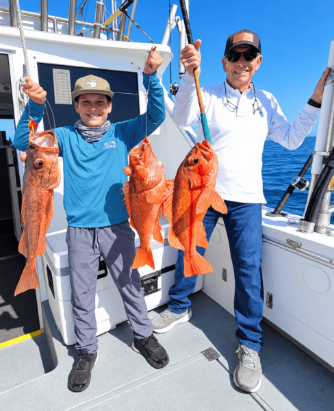 Two people holding red snapper fish on a boat in Santa Cruz.