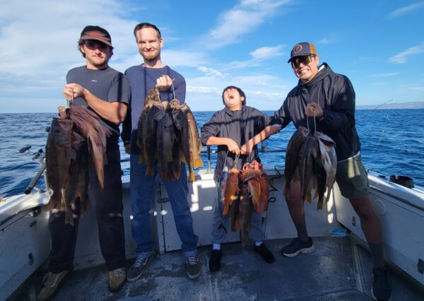 Group of four people holding their catch on a boat in Santa Cruz.