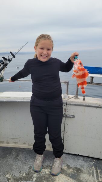Smiling girl holding a bright orange fish on a fishing boat.