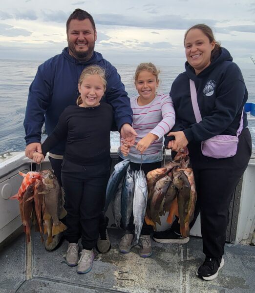 Family holding caught fish on a boat during a fishing trip in Monterey Bay.